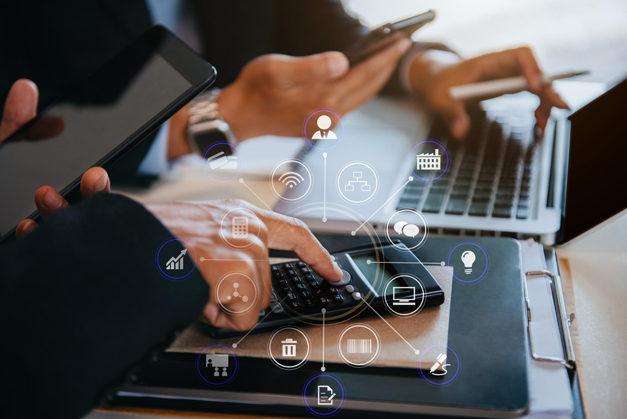 Pessoas trabalhando com laptop, tablet e calculadora, enquanto ícones digitais de processos empresariais e tecnologia aparecem sobrepostos à imagem. Imagem de capa para o blogpost Reforma Tributária 2026: Como Preparar Seu ERP Antes Que Seja Tarde Demais