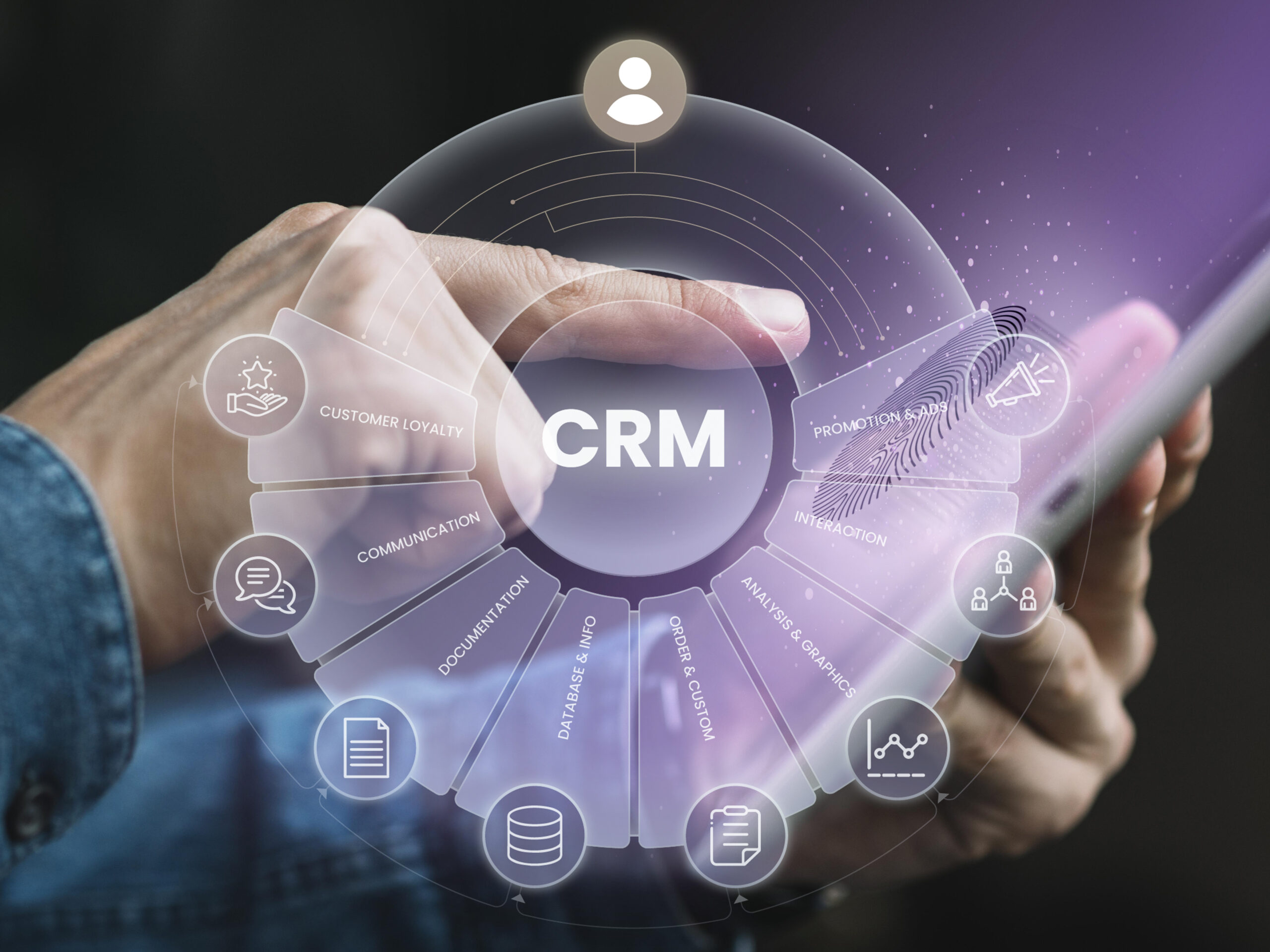 Imagem de capa para o blogpost Mão segurando um smartphone com uma interface holográfica de CRM (Customer Relationship Management), exibindo ícones de comunicação, fidelização de clientes, análise de dados, interações e campanhas promocionais, representando gestão do relacionamento com clientes e uso de tecnologia digital.